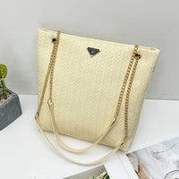 Beige woven tote bag with gold chain straps on white table, modern minimalist style
