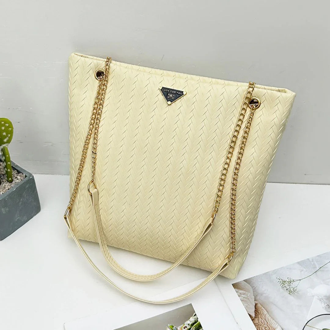 Beige woven tote bag with gold chain straps on white table, modern minimalist style