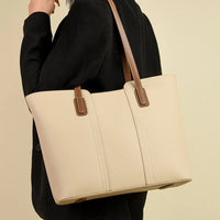 Beige leather tote bag with brown handles carried by person in black blazer