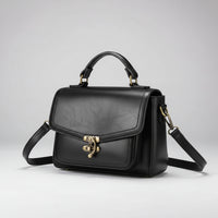 Black leather handbag with gold hardware and adjustable strap on a light background