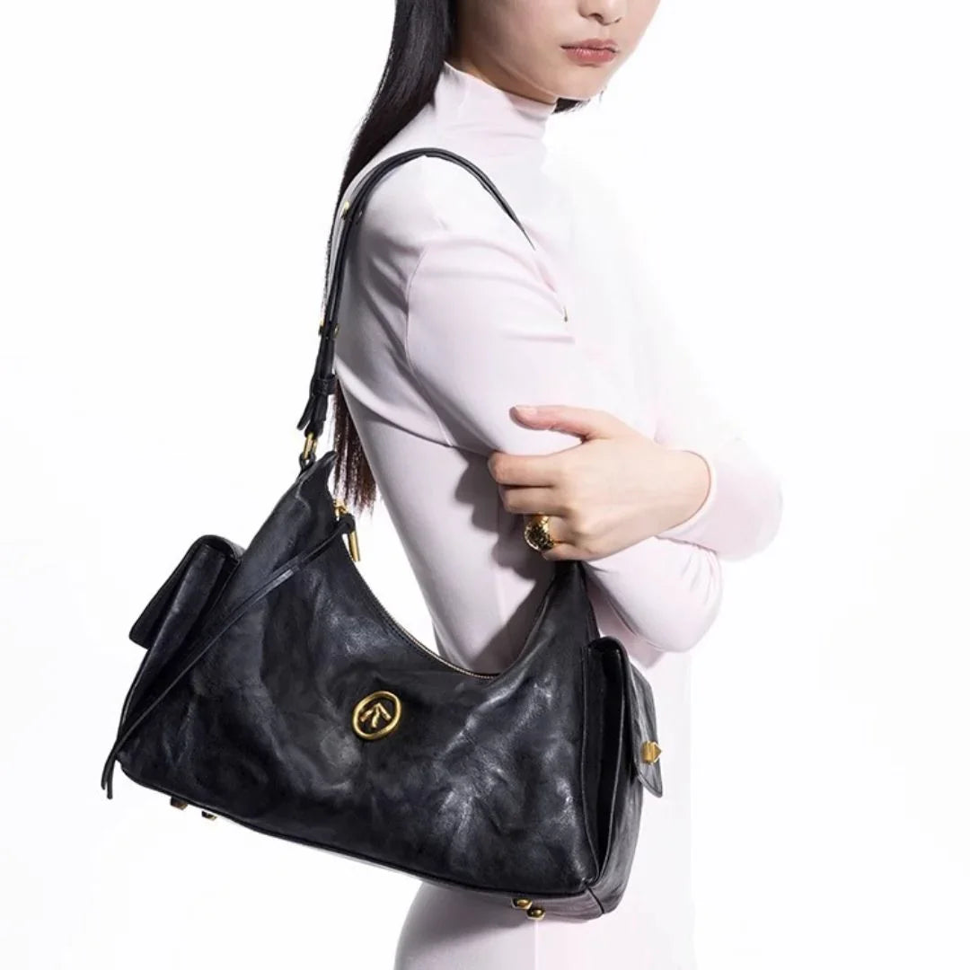 Woman in white turtleneck holding black leather shoulder bag with gold hardware