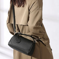 Woman in beige trench coat carrying a black leather crossbody bag