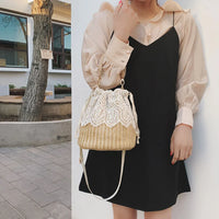 Woman in beige blouse and black dress holding a straw lace bucket bag outdoors
