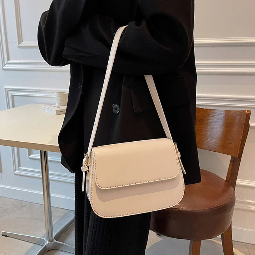 Beige leather crossbody bag worn over black blazer in modern cafe setting
