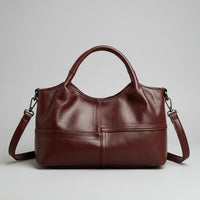 Burgundy leather handbag with double handles and detachable shoulder strap on gray background