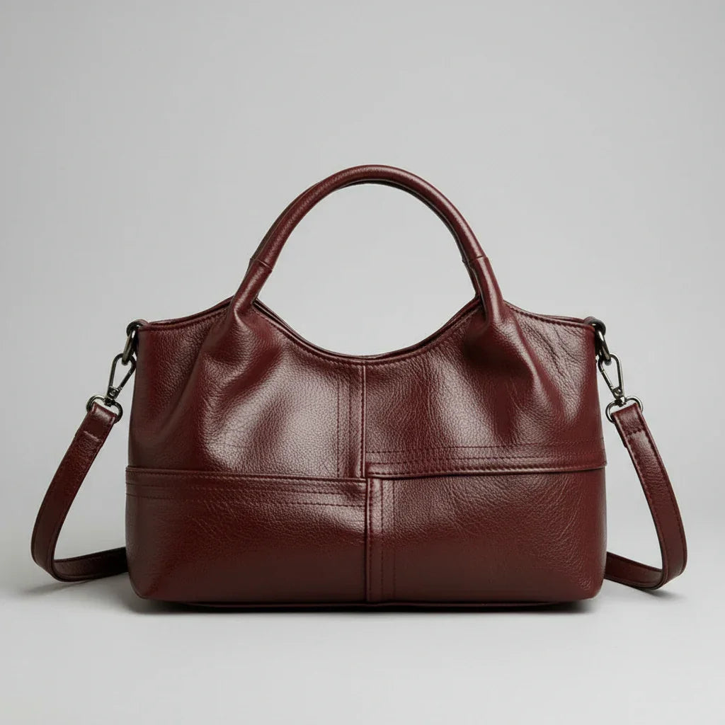 Burgundy leather handbag with double handles and detachable shoulder strap on gray background