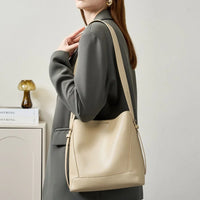 Woman in grey blazer carrying beige leather shoulder bag, minimal modern decor background