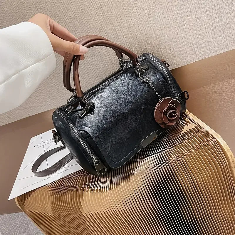 Black leather handbag with brown handles and rose charm on a modern chair