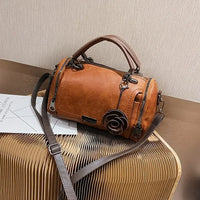 Brown leather handbag with flower charm and dual handles on a modern textured table