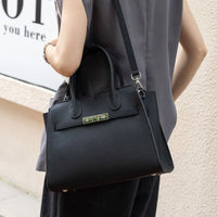 Woman carrying black leather handbag with gold clasp and shoulder strap outdoors