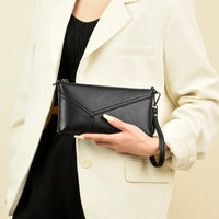 Woman in white blazer holding black leather clutch purse with wrist strap