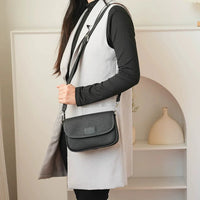 Woman wearing a black crossbody bag and grey vest in modern indoor setting