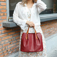 Woman holding large red leather tote bag, floral dress, white blouse, brick wall background