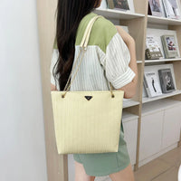 Woman with long hair carrying a beige woven tote bag with gold chain straps in a modern bookstore