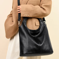 Woman wearing tan blazer and holding large black leather shoulder bag