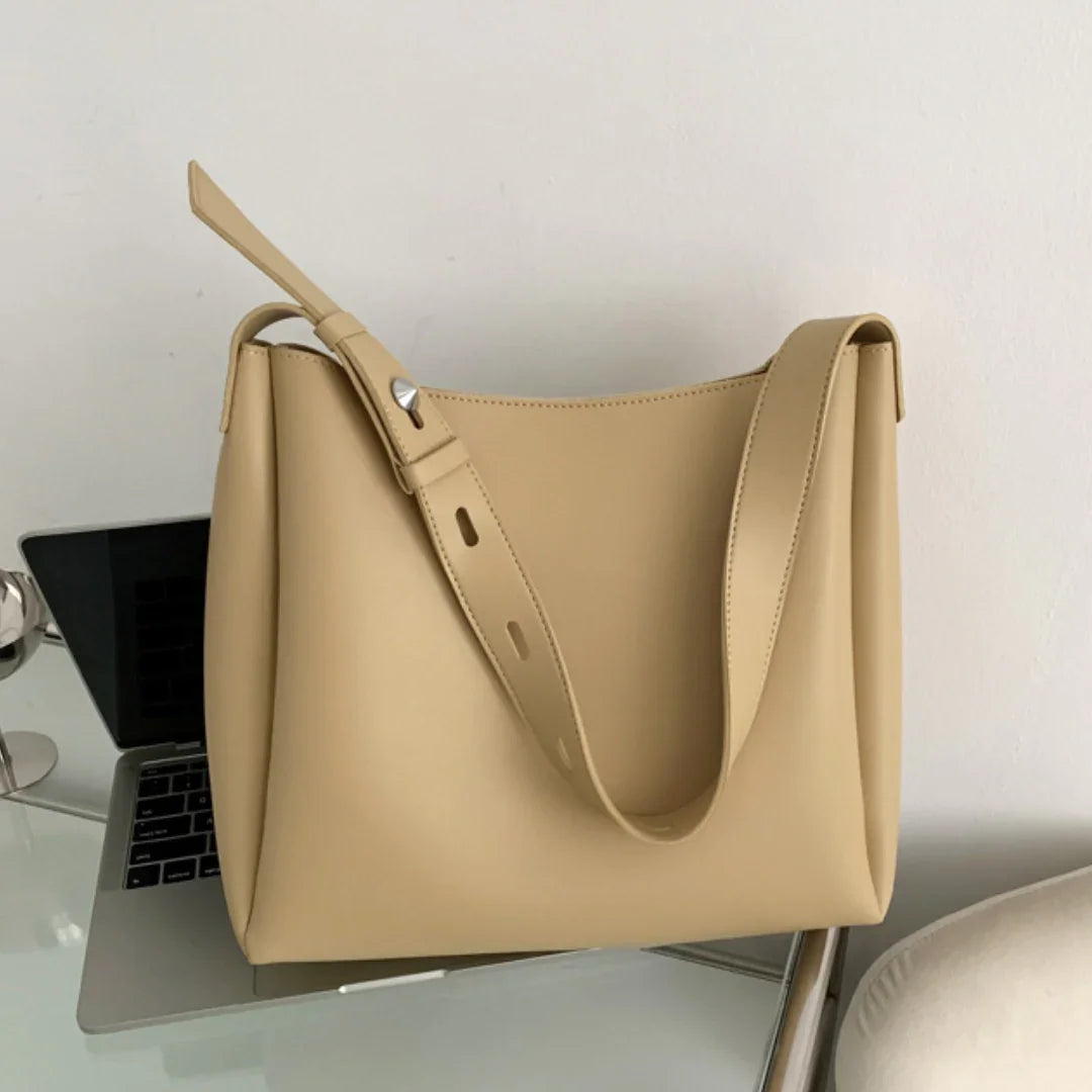 Beige leather tote bag with adjustable strap on glass desk near laptop