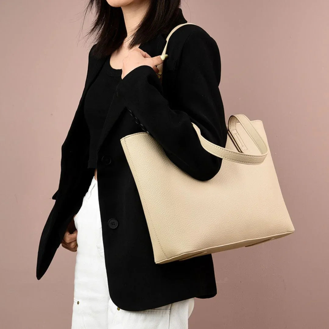 Woman wearing black blazer and white pants holding large beige leather tote bag