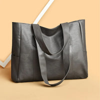 Gray leather tote bag with shoulder straps on beige background