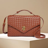 Brown woven leather crossbody bag with gold clasp on beige pedestal