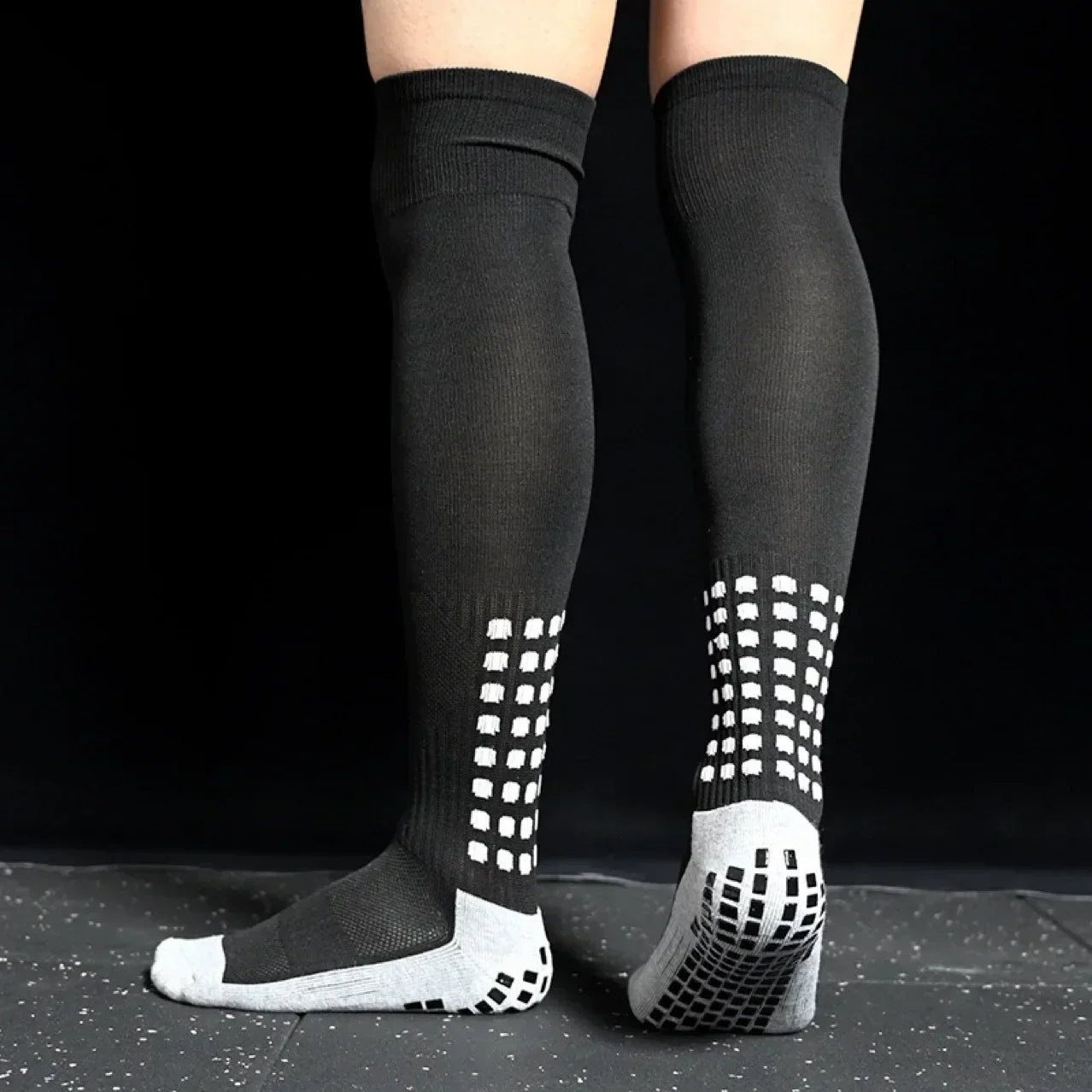 Black knee-high socks with white textured sole on a black background