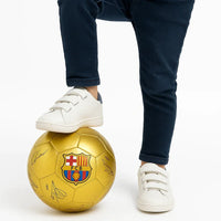 Gold soccer ball with FC Barcelona logo and signatures, by a person on a white background