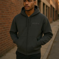 Man wearing a dark hoodie with 'BELIEVE' text, standing against a brick wall.