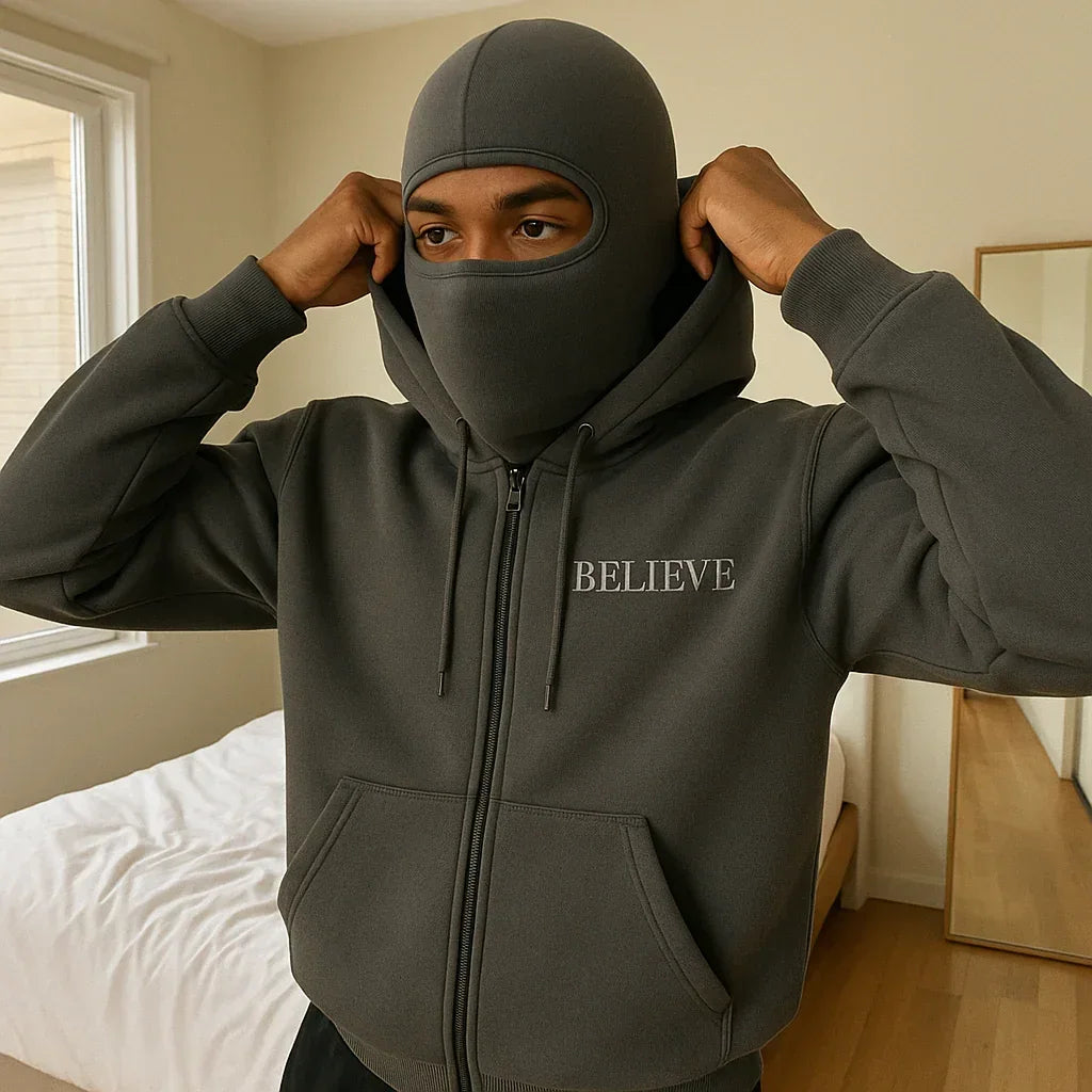 Person wearing a dark gray hoodie with 'BELIEVE' text, standing in a room.
