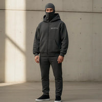 Person wearing a dark gray hoodie and pants with 'BELIEVE' text, standing against a concrete wall.