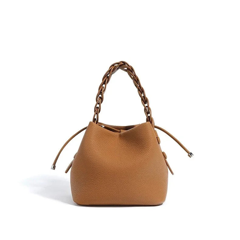 Brown leather bucket bag with drawstring closure and braided handle on white background