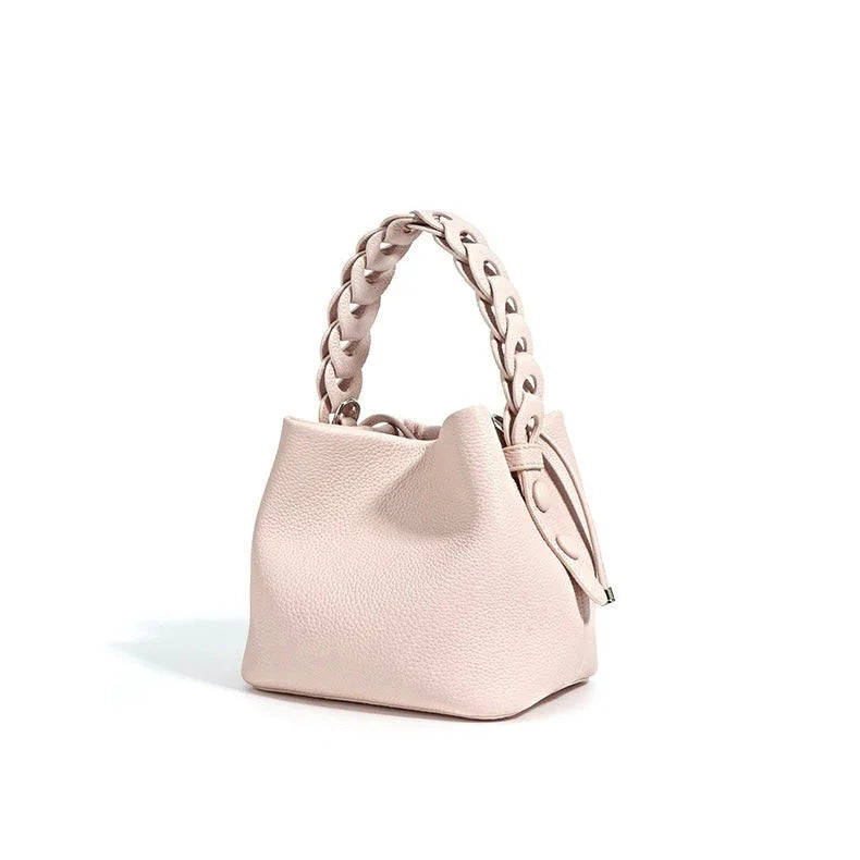 Light pink leather handbag with braided handle on white background