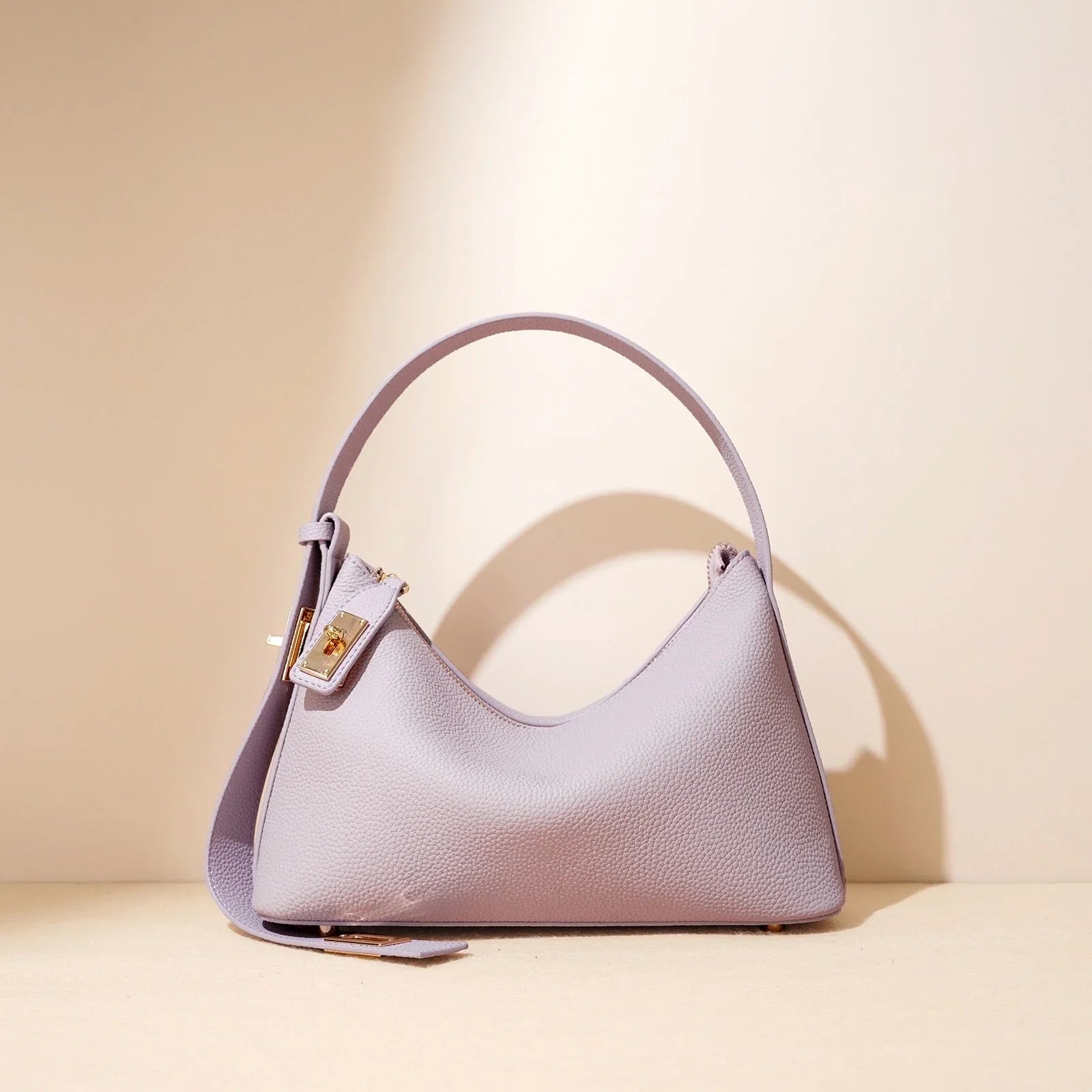 Lilac leather shoulder bag with gold buckle on beige background