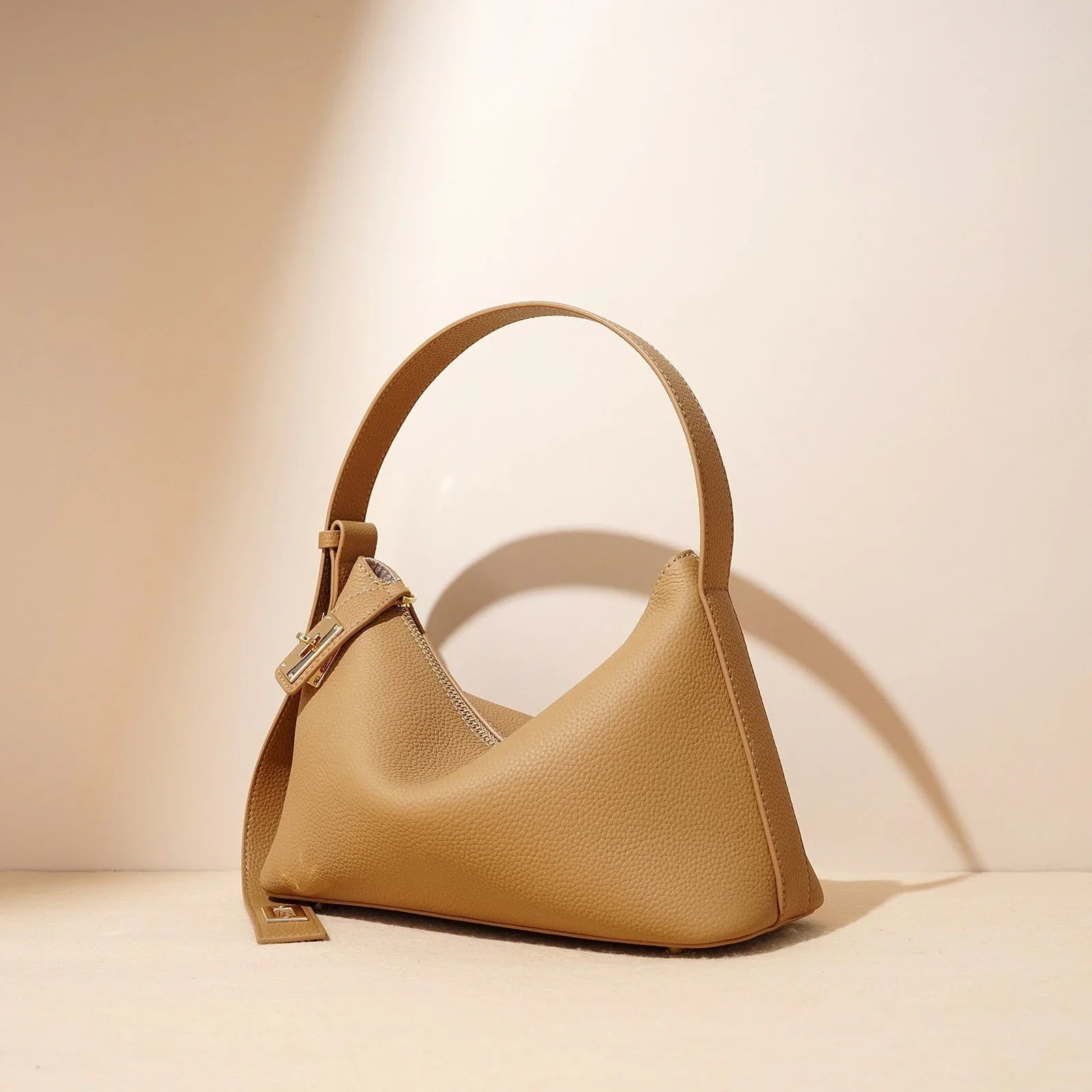 Beige leather handbag with gold clasp on neutral background, minimalist fashion accessory