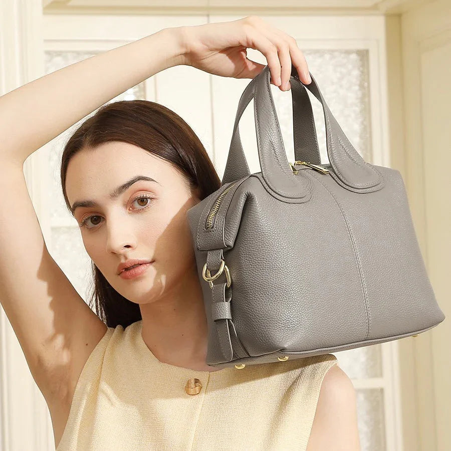 Woman holding a gray leather handbag with gold hardware in a bright indoor setting