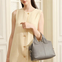 Woman in sleeveless cream dress holding a gray leather handbag indoors