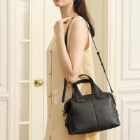 Woman in beige dress carrying black leather handbag with shoulder strap indoors