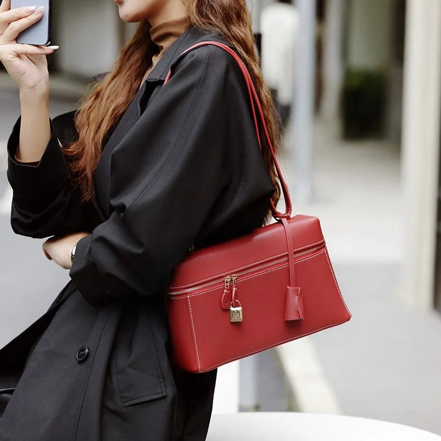 Woman in black coat carrying a red leather shoulder bag with gold zipper and lock