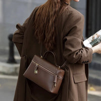 Woman in brown blazer carrying stylish brown leather shoulder bag outdoors