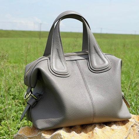 Gray leather handbag on a rock outdoors, stylish purse in grassy field