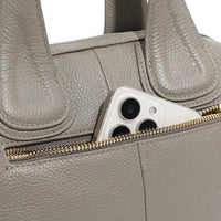 Beige leather handbag with gold zipper pocket holding a smartphone