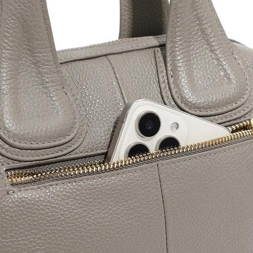 Beige leather handbag with gold zipper pocket holding a smartphone