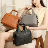 Woman in cream dress displaying brown, gray, and black leather handbags on chair indoors