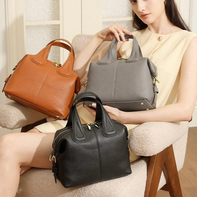 Woman in cream dress displaying brown, gray, and black leather handbags on chair indoors