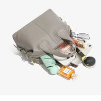 Gray leather handbag with makeup, perfume, glasses, tablet, and wallet spilling out