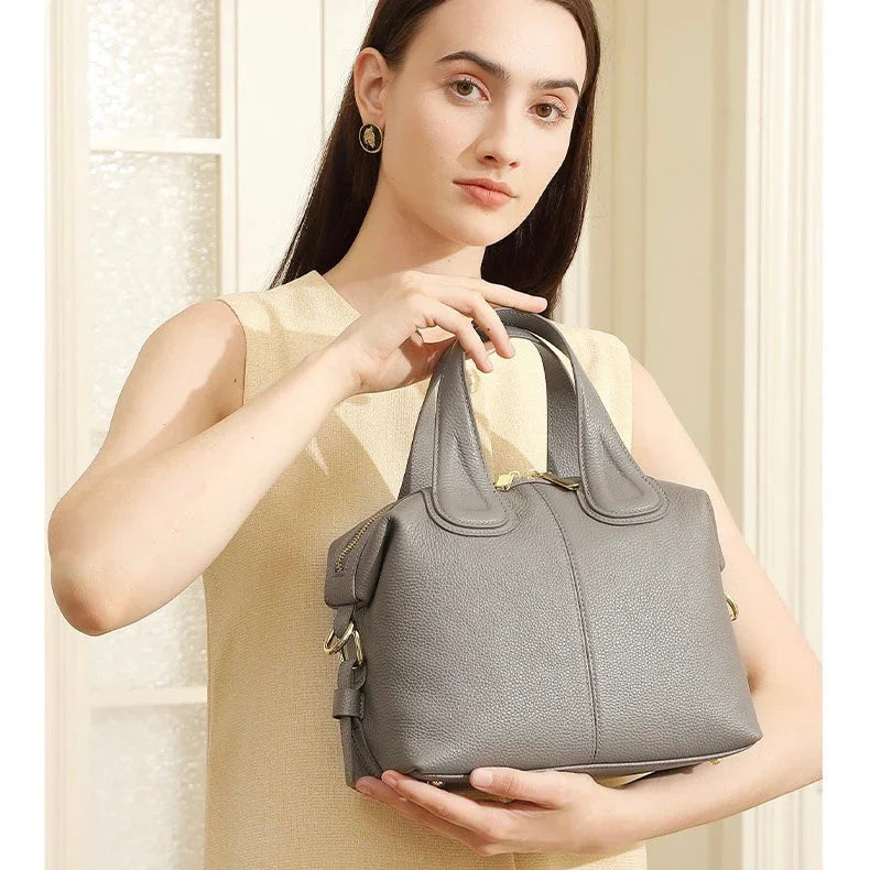 Woman in beige dress holding gray leather handbag in bright indoor setting