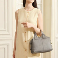Woman in sleeveless beige dress holding gray leather handbag indoors