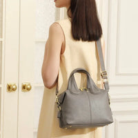 Woman wearing a sleeveless beige dress with a gray leather shoulder bag indoors