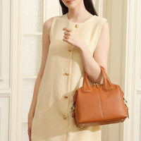 Woman in cream sleeveless dress holding a brown leather handbag indoors