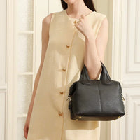 Woman in beige dress holding black leather handbag in elegant indoor setting