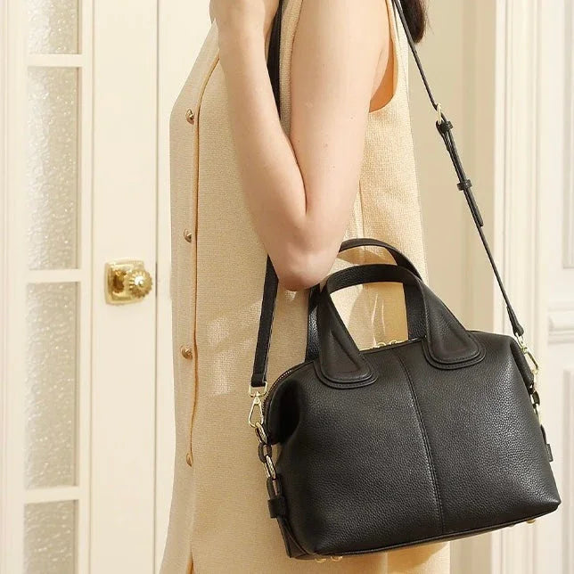 Woman in beige dress carrying a black leather crossbody handbag indoors