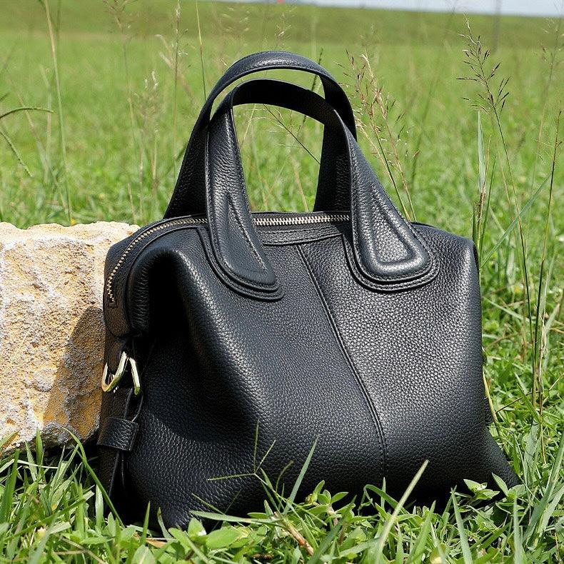 Black leather handbag on grass near a stone, outdoor fashion accessory product photo
